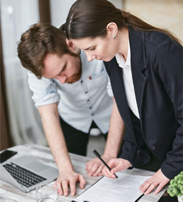 Dos profesionales revisando y firmando documentos en oficina con portátil, trabajo en equipo y gestión administrativa