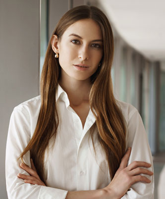 Mujer joven con camisa blanca y brazos cruzados en un pasillo de oficina, imagen corporativa profesional