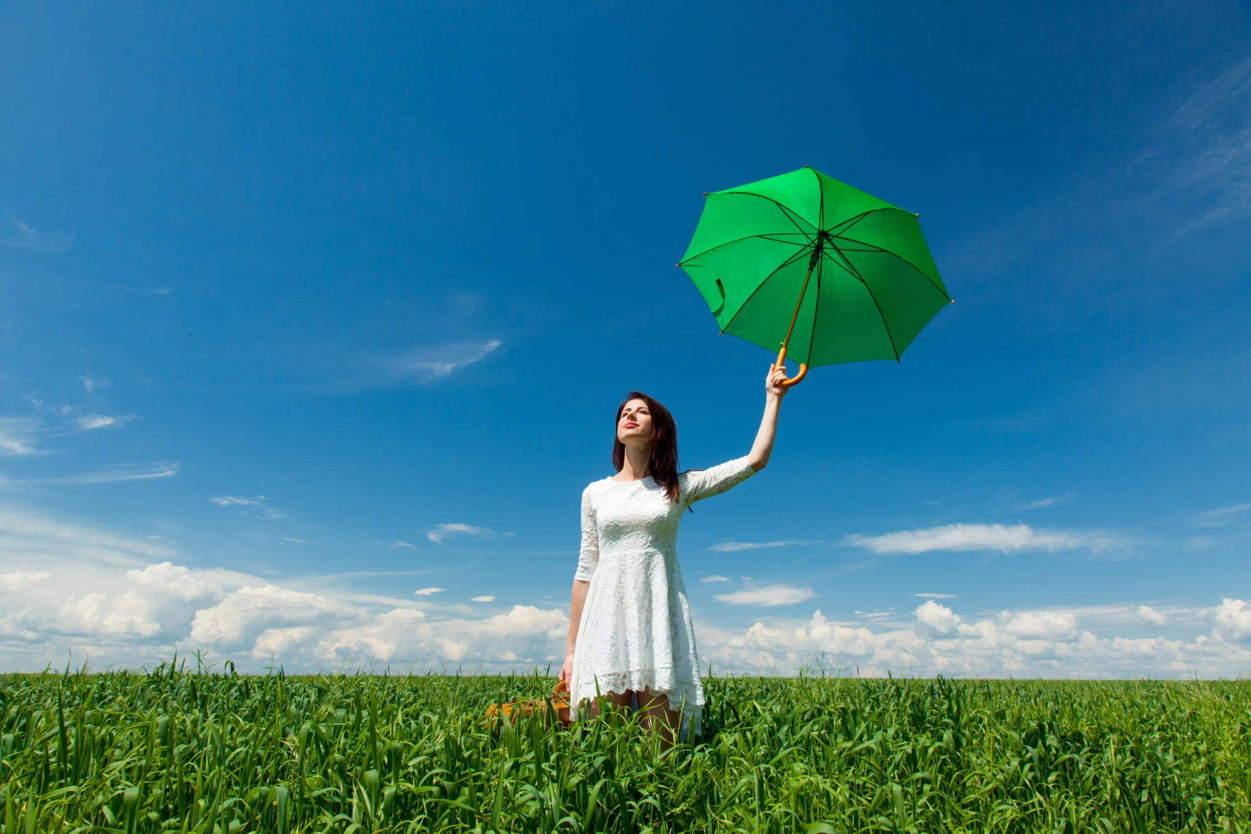 Mujer joven en la naturaleza sosteniendo un paraguas verde como símbolo visual de protección personal y bienestar