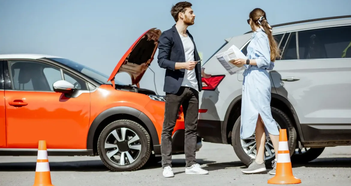 Accidente de tráfico entre un coche rojo y un SUV gris, con un hombre y una mujer intercambiando datos junto a conos de seguridad.