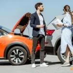 Accidente de tráfico entre un coche rojo y un SUV gris, con un hombre y una mujer intercambiando datos junto a conos de seguridad.