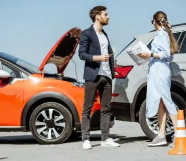 Accidente de tráfico entre un coche rojo y un SUV gris, con un hombre y una mujer intercambiando datos junto a conos de seguridad.