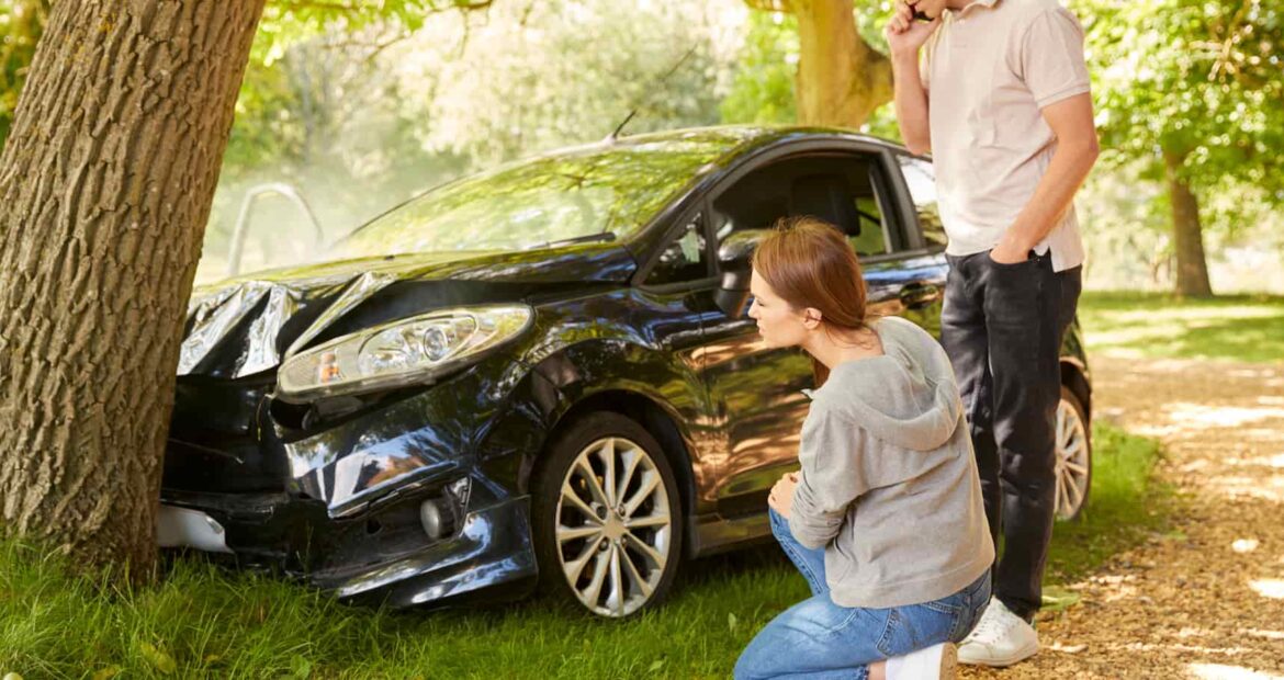 Coche dañado tras accidente contra un árbol con una pareja evaluando la situación en un entorno natural