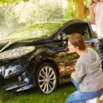 Coche dañado tras accidente contra un árbol con una pareja evaluando la situación en un entorno natural