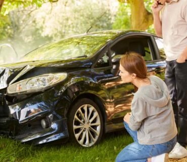 Coche dañado tras accidente contra un árbol con una pareja evaluando la situación en un entorno natural