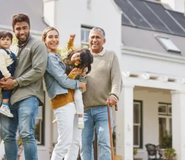 Familia de varias generaciones posando sonriente frente a una vivienda unifamiliar, representando la protección y seguridad del hogar con un seguro adecuado.