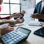 Asesor de seguros explicando el cálculo del capital asegurado a un cliente con documentos y calculadora sobre la mesa.