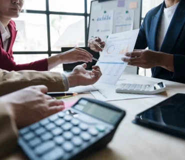 Asesor de seguros explicando el cálculo del capital asegurado a un cliente con documentos y calculadora sobre la mesa.