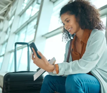 Un billete de viaje, un teléfono y una mujer negra en el aeropuerto, en una videollamada, esperando el avión y el vuelo.