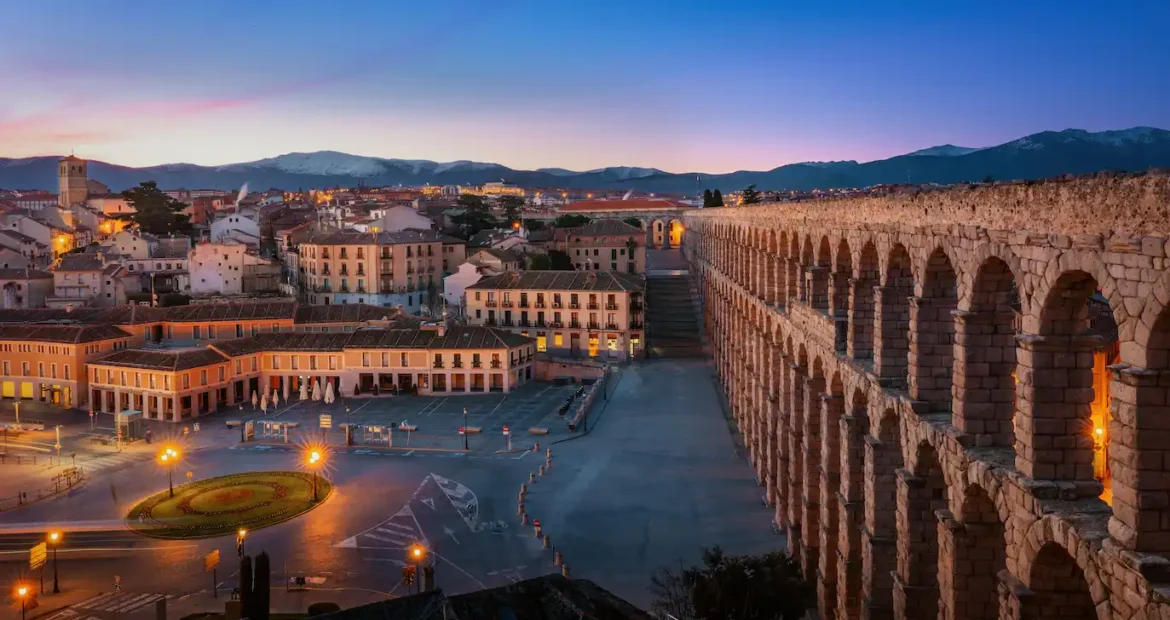 Acueducto de Segovia al atardecer con viviendas antiguas del casco histórico en primer plano.