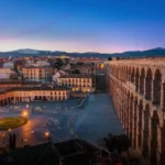 Acueducto de Segovia al atardecer con viviendas antiguas del casco histórico en primer plano.