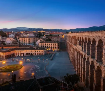 Acueducto de Segovia al atardecer con viviendas antiguas del casco histórico en primer plano.